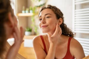 Woman looking in the mirror, touching her face while checking skin concerns like pimples, wrinkles, and under-eye bags, highlighting PRF treatment benefits for rejuvenation