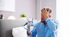 Shocked young man holding a CPAP mask, considering NightLase® treatment for sleep apnea as a non-invasive alternative for improved breathing and sleep quality