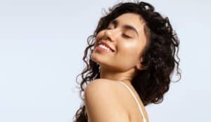 Smiling woman with clear, glowing skin and natural curly hair, representing the rejuvenating effects of PDF injection treatments for healthy, radiant skin