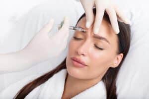 Young woman receiving a Botox injection in her forehead from a professional cosmetologist, highlighting anti-aging and wrinkle reduction treatments