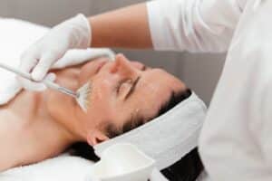 Woman receiving anti-aging facial chemical peel with retinol mask at beauty salon, concept of skin rejuvenation and wellness care.